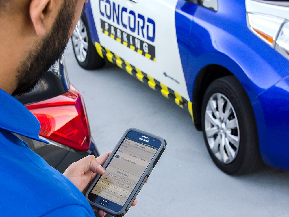 A concord employee looking at his smartphone while standing infront of his work vehicle